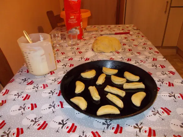 Ein schwarzes Backblech liegt auf einem weihnachtlich gedeckten Tisch mit ungebackenen Muschelplätzchen neben Teig und Mehl.