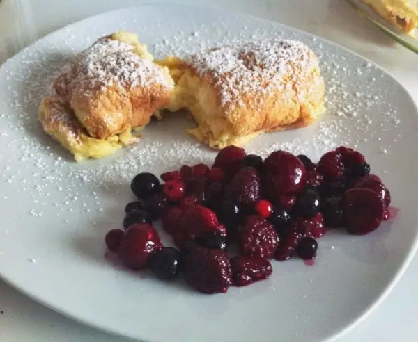 Zwei fluffige Salzburger Nockerl mit Puderzucker liegen auf einem Teller, begleitet von frischen Beeren.