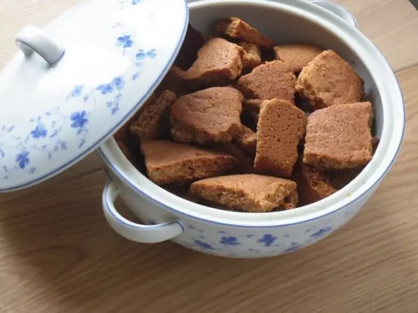 Ein gefüllter Topf mit Honiglebkuchen-Bruch steht auf einem Holztisch, bereit zum Servieren und Genießen.