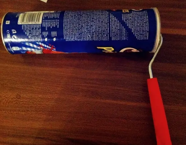 Ein Farbroller liegt auf einer Holzoberfläche, umgeben von einem blauen Farbdose, um ihn vor dem Austrocknen zu schützen.