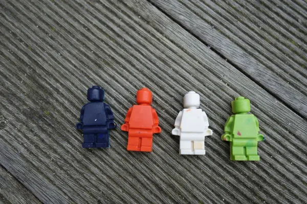 Bunte Wachsmalstifte in Form von Figuren liegen auf einer Holzoberfläche, bereit zum Schmelzen.