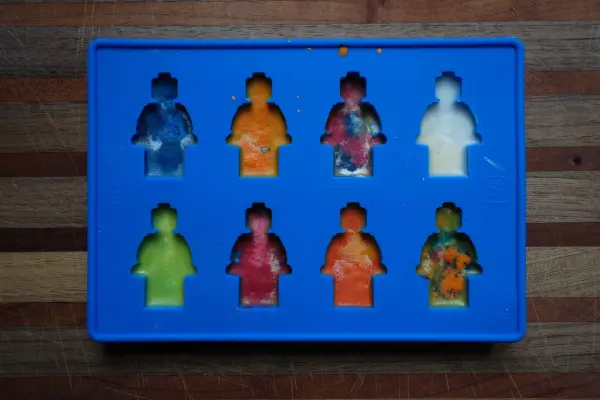 Bunte Wachsmalstifte, in Form von Figuren, sind in einer blauen Form angeordnet, ideal zum Schmelzen und Kreativsein.