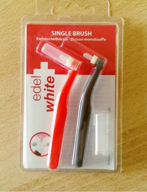 Einbüschelbürsten in einer Verpackung, zeigen zwei kleine Zahnbürsten in rot und schwarz für eine gezielte Zahnreinigung.