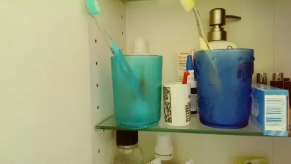 Ein grüner und ein blauer Becher stehen auf einem Regal, beide enthalten Einbüschelbürsten zur Zahnpflege.