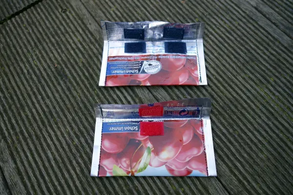 Mini-Portemonnaies aus Capri-Sonne liegen auf einem Holzbrett, ihre bunten Farben kontrastieren mit dem natürlichen Untergrund.