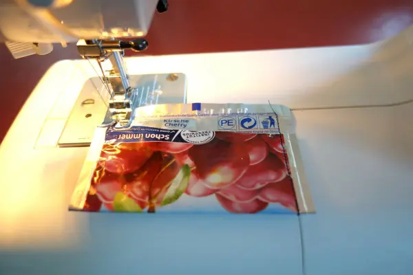 Ein Mini-Portemonnaie aus Capri-Sonne wird auf einer Nähmaschine gefertigt, während es auf einem weißen Tisch liegt.