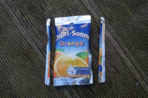 Ein Mini-Portemonnaie aus Capri-Sonne liegt auf einer Holzoberfläche, umgeben von zwei Strohhalmen.