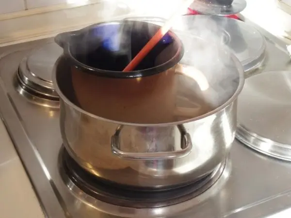 Ein Topf mit Schokolade wird auf dem Herd geschmolzen, während Dampf aufsteigt und ein Holzlöffel zum Rühren eingesetzt wird.