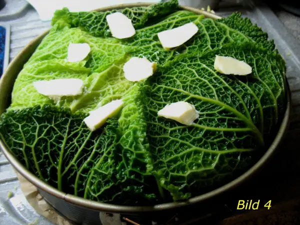 Ein gefüllter Wirsingkohl-Auflauf wird in einer runden Form vorbereitet, bedeckt mit frischem Wirsing und Butterstückchen.