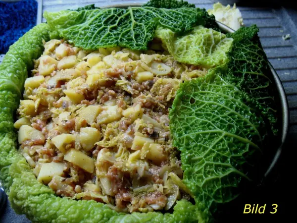 Gefüllter Wirsingkohl liegt auf einem Teller, mit einer Füllung aus Kartoffeln und Fleisch, umgeben von frischen Wirsingblättern.
