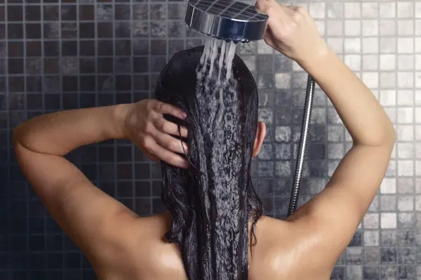 Eine Person wäscht sich im Duschraum die Haare mit Shampoo unter einem Wasserstrahl, um Shampoo zu sparen.
