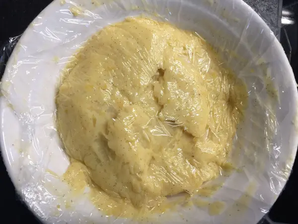 Ein glatter Teig für den russischen Schokoladenzopf ruht in einer Schüssel, mit Folie abgedeckt, bereit zum Aufgehen.