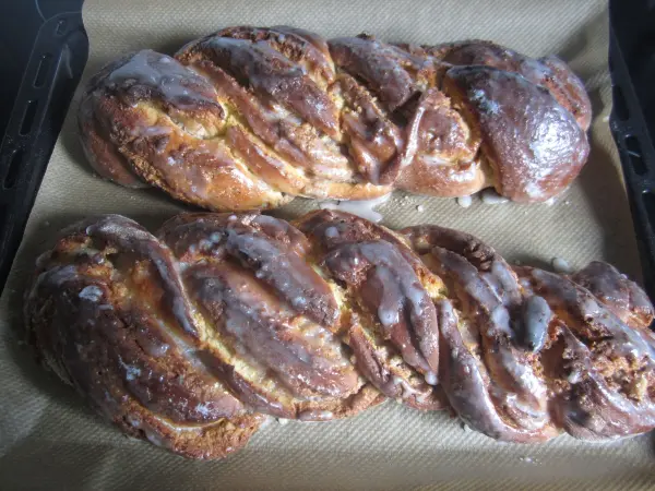 Ein rustikaler Schokoladenzopf liegt frisch gebacken auf einem Blech, umgeben von Backpapier, mit glänzender Kruste.
