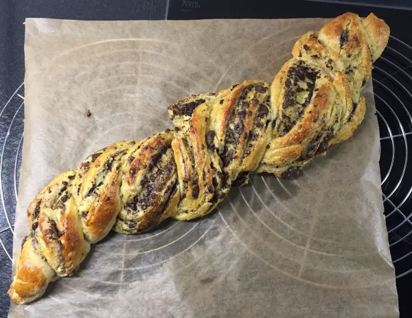 Ein frisch gebackener Schokoladenzopf liegt auf Backpapier und präsentiert seine goldenen, schokoladigen Stränge.