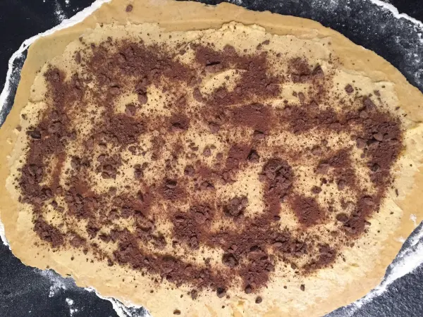 Ein Schokoladenteig liegt auf einer Oberfläche und ist mit Kakaopulver bestreut, bereit für den nächsten Schritt.