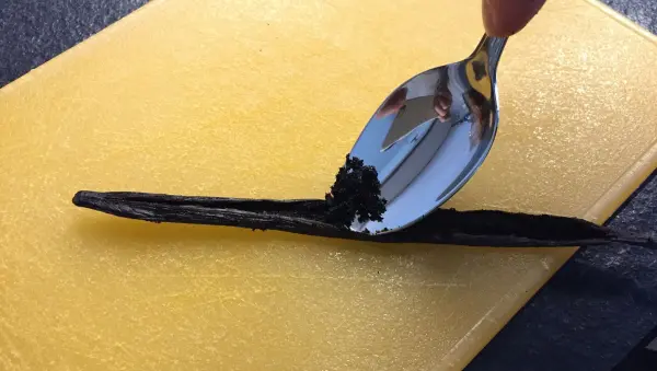 Ein Löffel kratzt Vanille aus einer Schote, während diese auf einem gelben Schneidebrett liegt, bereit für den Schokoladenzopf.