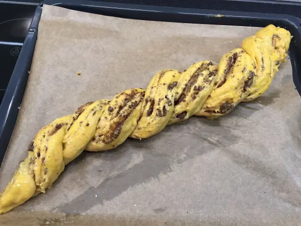 Ein frisch geflochtener Schokoladenzopf liegt auf Backpapier in einer Backform, bereit zum Backen.