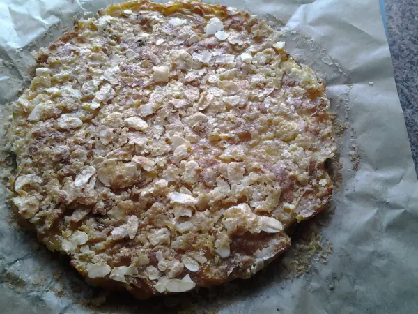 Ein Apfelkuchen liegt auf Backpapier, leicht braun mit Haferflocken und einer knusprigen Oberfläche in einer modernen Küche.