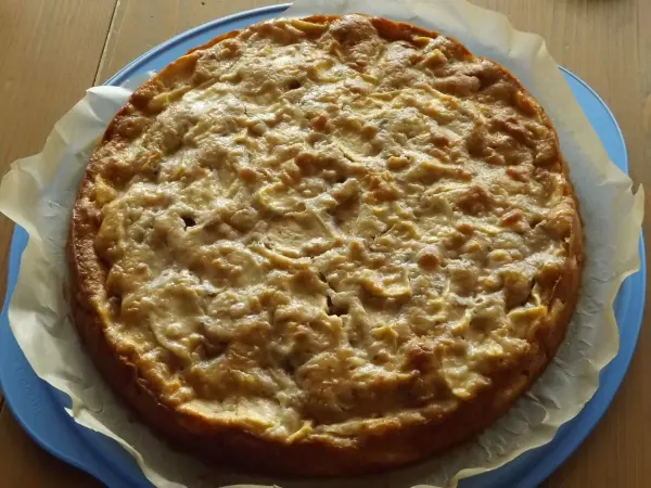 Ein runder französischer Apfelkuchen liegt auf einem blauen Teller und präsentiert sich goldbraun und kross auf einem Tisch.