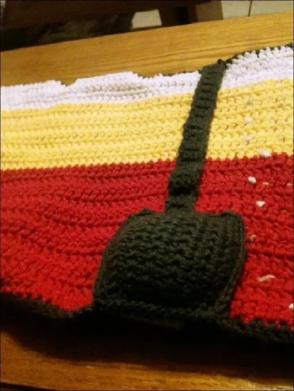 Ein gehäkelter Utensilo für Häkelnadeln liegt auf einem Holztisch und zeigt eine farbige, gestreifte Oberfläche mit Halter.