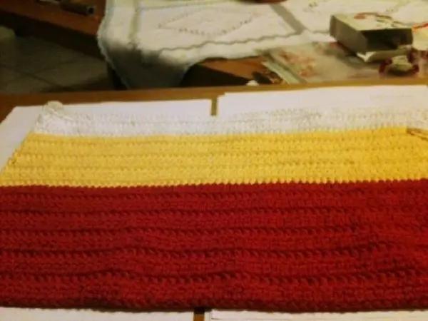 Ein gehäkeltes Utensilo liegt auf einem Tisch und zeigt bunte Streifen in Rot, Gelb und Weiß, bereit zur Nutzung.