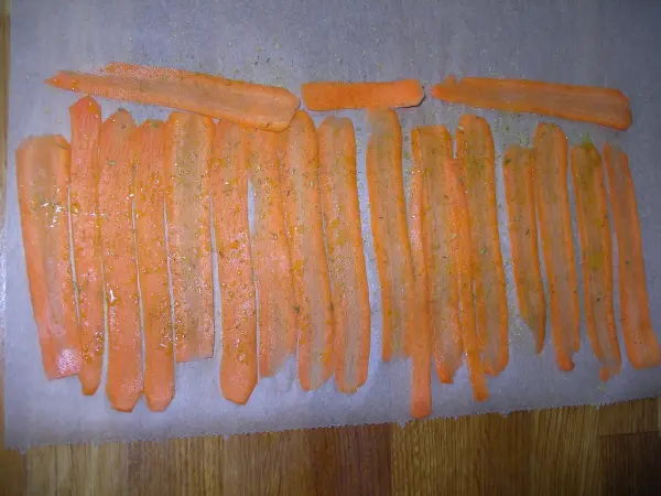 Auf einem Holzbrett liegen gleichmäßig geschnittene Möhrenchips, die bereit sind, zum Rösten in die Küche zu gelangen.