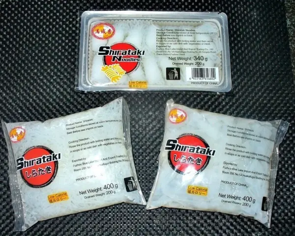 Shirataki-Nudeln aus Konjakwurzel liegen verpackt auf einer dunklen Oberfläche, bereit zur Verwendung in der Küche.