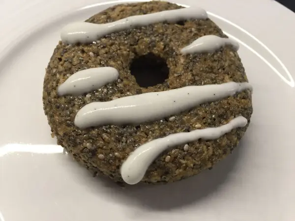 Ein Chia-Donut mit einer glänzenden, weißen Zitronen-Kokos-Creme-Dekoration liegt auf einem weißen Teller.