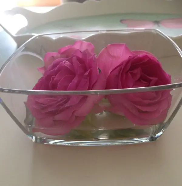 Zwei rosa Rosen liegen in einer klaren Glasvase im Wasser, umgeben von hellen, sanften Farbtönen.