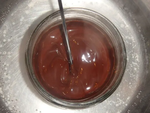Eine Schüssel enthält geschmolzene dunkle Schokolade, während ein Löffel sie umrührt, bereit für Sesamsalzstangen.