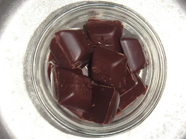 Dunkle Schokolade liegt in einem klaren Glas. Sie sind gleichmäßig geschnitten und glänzen, bereit zum Schmelzen.