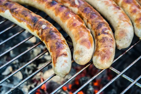 Gegrillte Würstchen liegen auf einem Rost über glühender Kohle und zeigen appetitliche Grillspuren, ideal für ein BBQ.