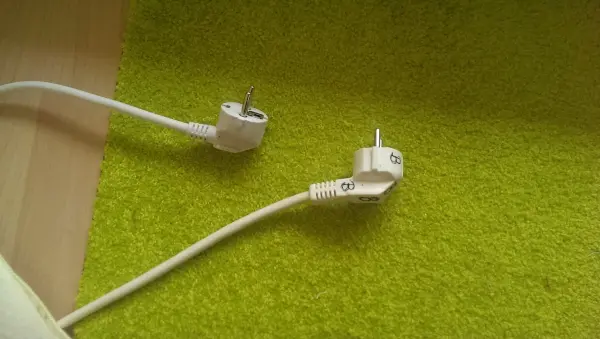 Ein Bügeleisenkabel liegt auf einem grünen Teppich, der Stecker ist abgezogen, um die Sicherheit beim Verlassen der Wohnung zu gewährleisten.