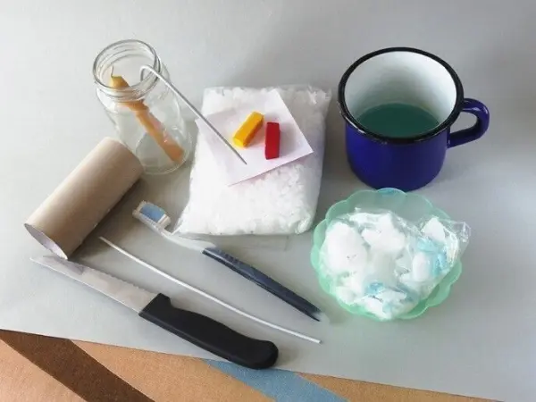 Materialien zum Sandkerzen basteln liegen auf einem Tisch: Wachs, Farben, Dochte und Werkzeuge zur Herstellung.