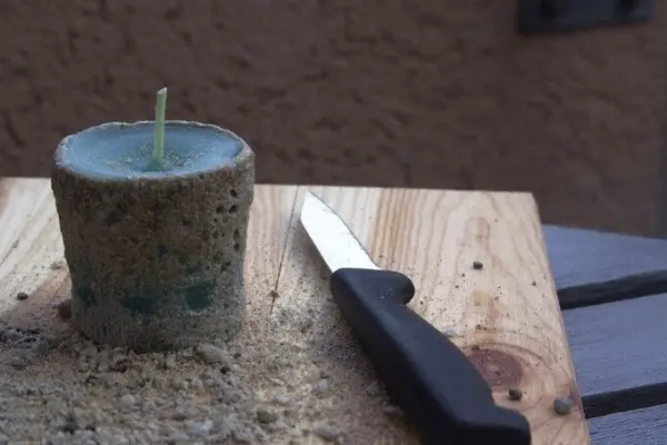 Eine Sandkerze steht auf einem Tisch, während ein Messer daneben liegt, um sie weiter zu bearbeiten.