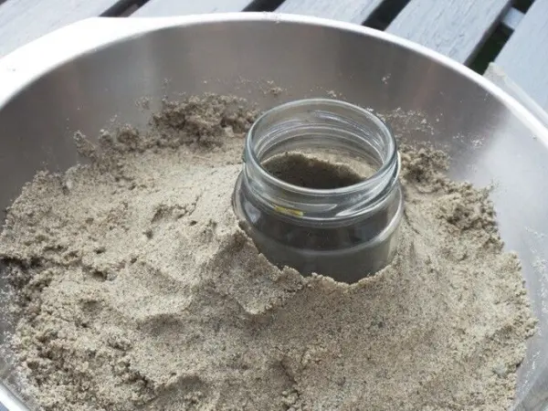 Eine Glasform steht in der Mitte von Sand, der zum Basteln von Sandkerzen genutzt wird.