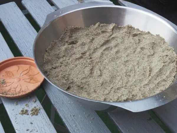 In einer großen Schüssel liegt feiner Sand, um Sandkerzen zu basteln. Daneben steht eine kleine Schale mit einer Blütenform.