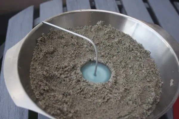 In einer Schüssel mit Sand steht eine Sandkerze im Entstehen, während der Docht mittig positioniert ist.