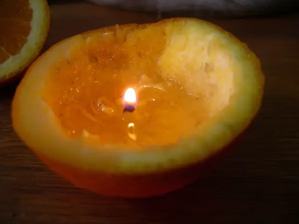 Eine Öllampe in einer Orangenschale brennt sanft auf einem Tisch, umgeben von natürlichen Materialien und sanftem Licht.