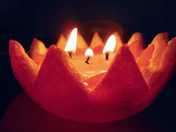 Eine Öllampe in einer Orangenschale brennt, während sie in einem dunklen Raum sanft leuchtet und stimmungsvolles Licht verbreitet.