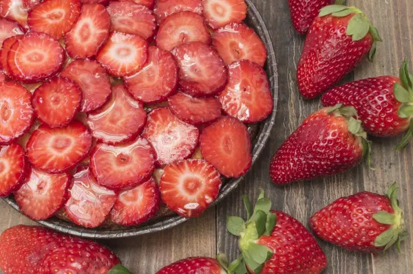Kreisrunde Obstkuchen mit frischen Erdbeeren, die auf einem Holzbrett schön angerichtet sind, umhüllt von Gelatine.