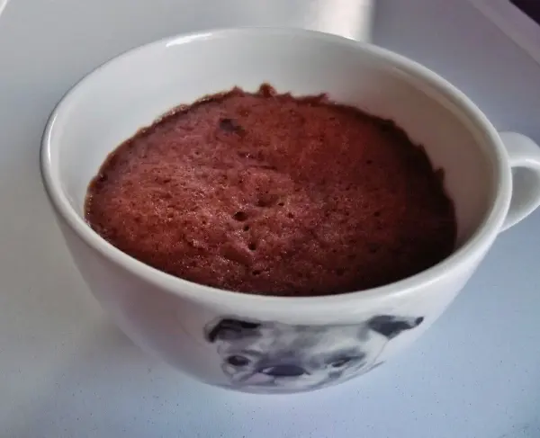 Eine Tasse mit Schoko Tassenkuchen steht auf einem Tisch, der Kuchen ist weich und luftig in der Tasse.