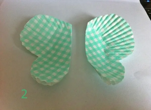 Zwei grüne Muffinformen in Schmetterlingsform liegen auf einem weißen Untergrund, bereit zum Basteln von Dekorationen.