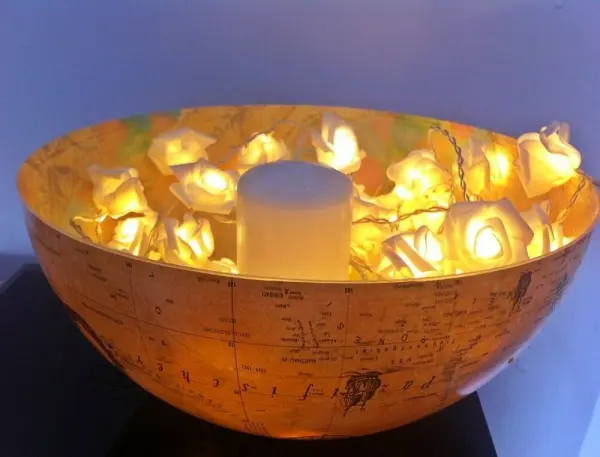 Ein alter Globus dient als Schale, beleuchtet von einem Kerzenhalter und umgeben von leuchtenden Blumen im Raum.