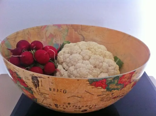 Ein alter Globus dient als Schale und ist mit Radieschen und Blumenkohl gefüllt, auf einem schwarzen Untergrund.