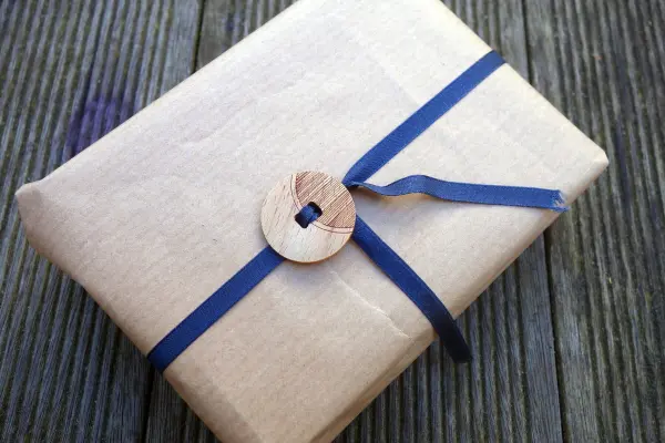 Ein Geschenk ist mit braunem Papier und blauer Schleife verpackt, dekoriert mit einem großen Holzknopf auf einem Holzgrund.