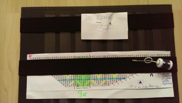 Ein Strickmusterblatt liegt auf einem Tisch, während eine Maschenprobe mit farbigen Markierungen darauf sichtbar ist.