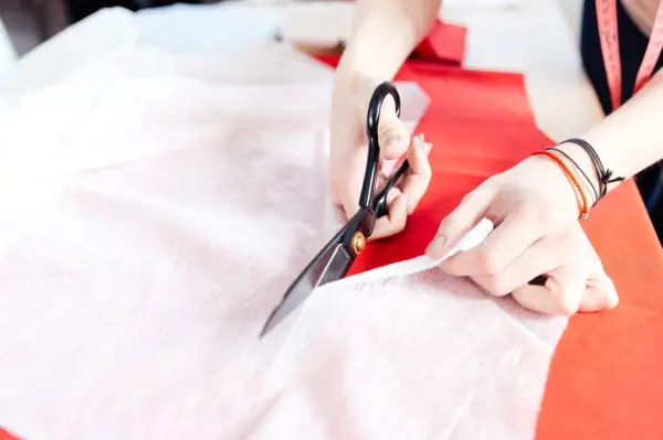 Eine Hand schneidet rutschigen Stoff mit einer Schere, während der Stoff auf einem roten Untergrund liegt.