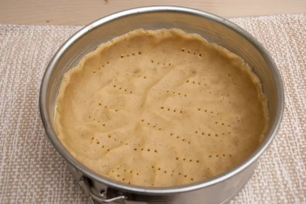 Ein ungebackener Kuchenteig liegt in einer runden Springform auf einem hellen Untergrund, bereit zum Backen.