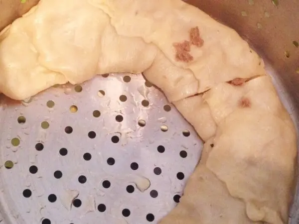 Eine Kirgisische Nudel-Hackfleischrolle wird in einem Dampfgarer gegart, umgeben von einem perforierten Einsatz für gleichmäßige Hitze.